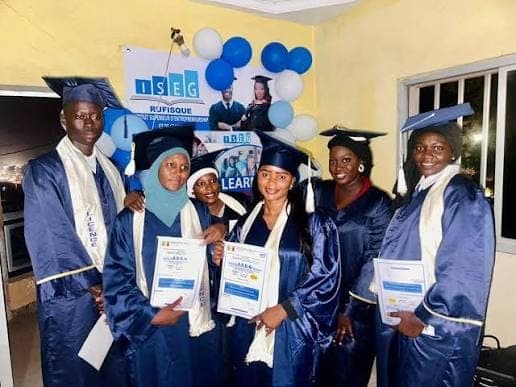 Sept diplômés de l’ISEG Rufisque en toge et toque, leur diplôme à la main, devant une banderole de l’école